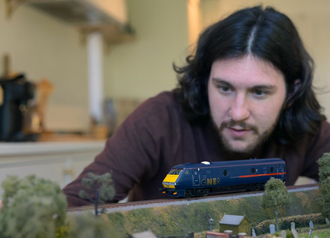 Man overlooking the model railway, focussing on the train. 